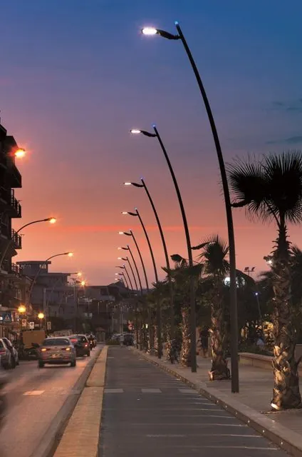 عمود إنارة شوارع معدني من أكتار يحمل كشّافاً حديثاً بتقنية LED على طريق، يوضّح مشروع تحويل الإنارة القديمة إلى LED مع باب الخدمة وعلبة الوصل