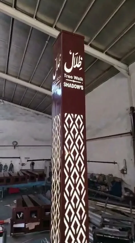 A brown laser-cut decorative lighting pole carrying the Tree Walk project logo, manufactured by Aktar, illuminated in the workshop